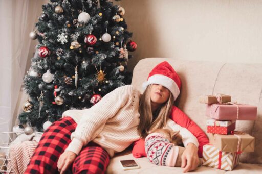 Frau schläft an Weihnachten erschöpft vor dem Tannenbaum ein