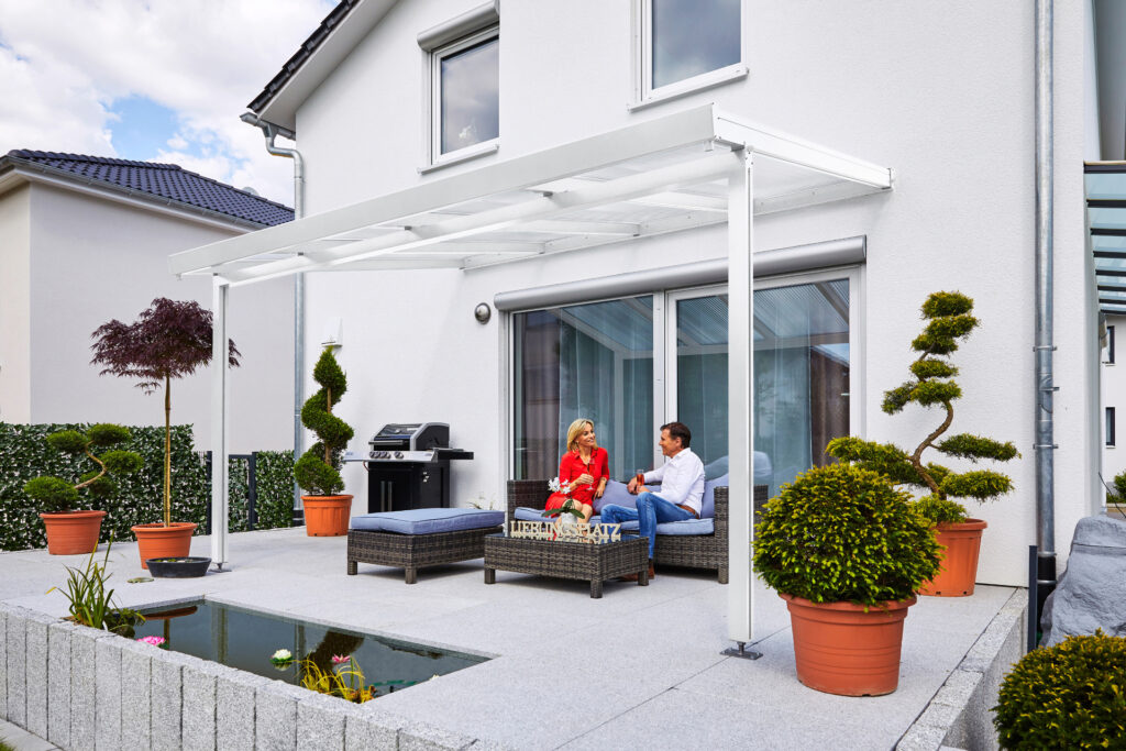 Terrassendach weiß, Frontansicht mit zwei Menschen auf Gartenmöbeln beim Kaffeetrinken