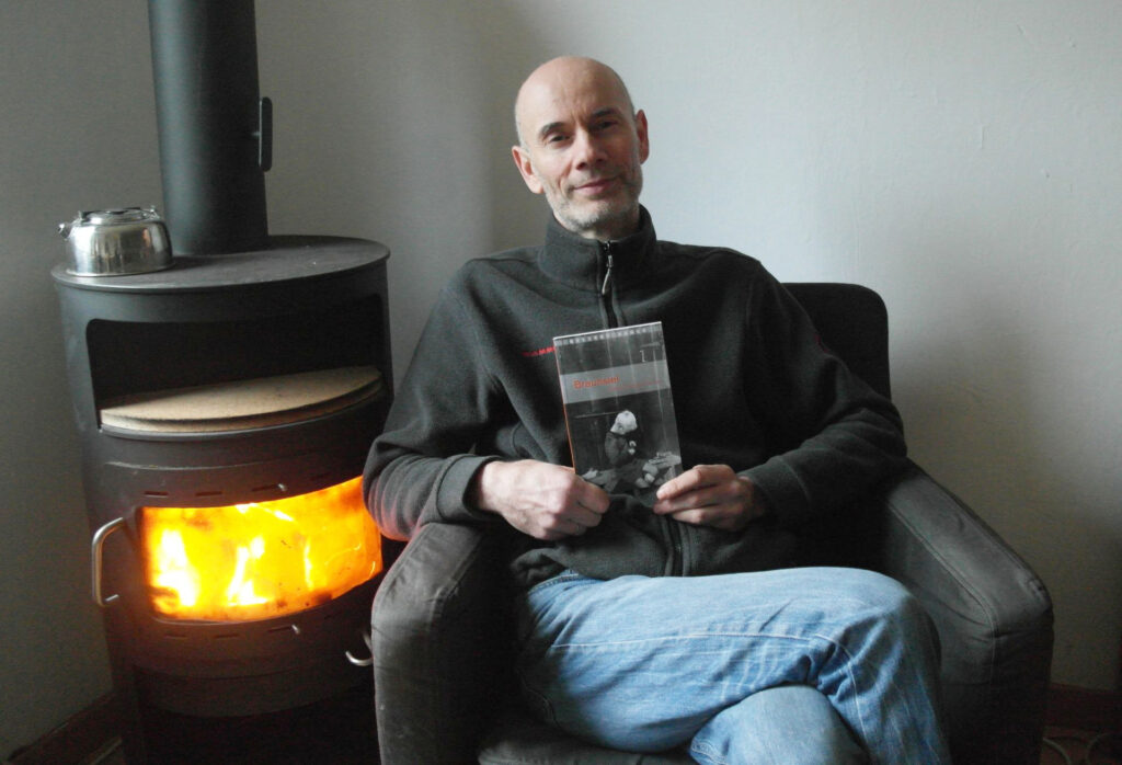 Frank Salewski sitzt am Kamin und präsentiert sein Buch "Braunsiel - Eine Dorfgeschichte"