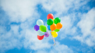 Luftballons schweben im Himmel vor Wolken