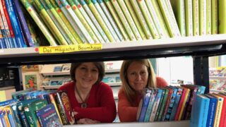 Die zwei Mitarbeiterinnen des QBZ Robinsbalje gucken durch ein Bücherregal durch