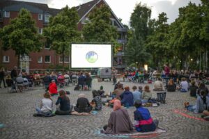 Menschen sitzen auf einem Platz und warten auf den Start vom Freiluftkino Gröpelingen