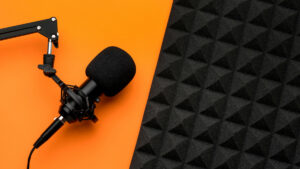 Nahaufnahme eines Mikrofons vor orangefarbenem Hintergrund und neben einer Akustikdämmung