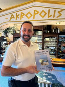 Christos Kalogirou präsentiert ein Fotobuch am Tresen seines Restaurants Akropolis in Bremen-Schwachhausen
