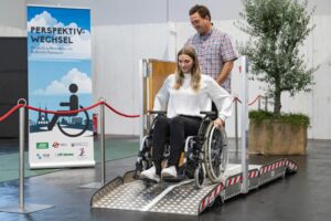 Eine Frau im Rollstuhl wird auf der Messe InVita von einem Mann testweise über eine Rampe gefahren.