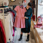 Symbolbild für Secondhandläden in Bremen: Eine trendig gekleidete Frau schaut ein Kleid in einem Secondhandladen an