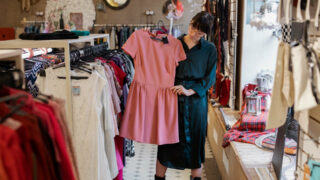 Symbolbild für Secondhandläden in Bremen: Eine trendig gekleidete Frau schaut ein Kleid in einem Secondhandladen an