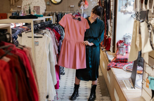 Symbolbild für Secondhandläden in Bremen: Eine trendig gekleidete Frau schaut ein Kleid in einem Secondhandladen an