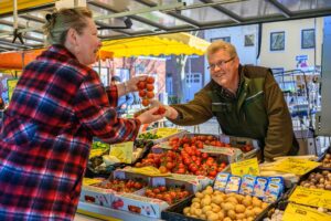 Wochenmarkt vom Großmarkt Bremen: Ein Händler überreicht einer Frau Tomaten am Strunk.