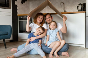 Symbolbild für energetische Sanierung eines Altbaus: Eine Familie mit kleinen Kindern hält sich eine Pappe wie ein Dach über den Kopf.