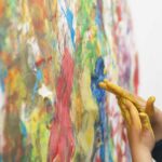 Kind mit Farbe an den Händen steht vor einer Leinwand