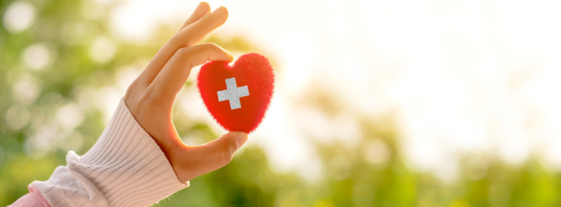 Eine Hand hält ein kleines rotes Herz mit weißem Kreuz hoch