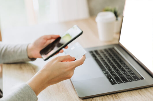Mensch hält ein Smartphone und eine Chipkarte vor einen Laptop