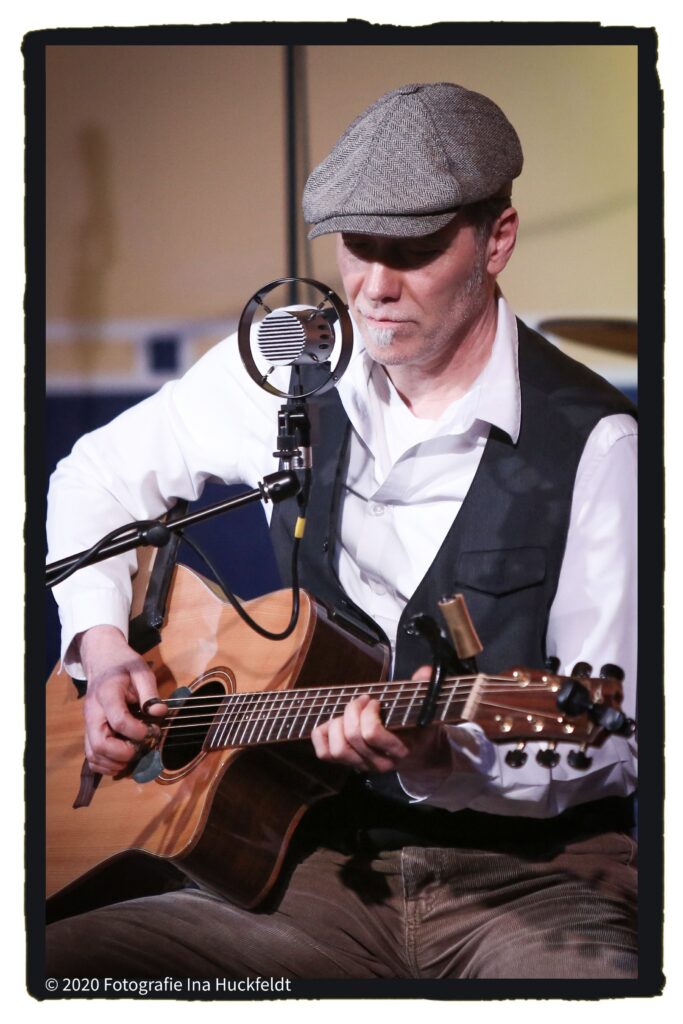 Mann mit Mütze ,Gitarre und Mikrofone