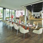 Blick in den modern eingerichteten Community-Bereich der Stadtteilfiliale Horn-Lehe der Sparkasse Bremen. Im Zentrum steht ein großer Tisch mit vielen Stühlen.