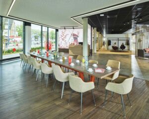 Blick in den modern eingerichteten Community-Bereich der Stadtteilfiliale Horn-Lehe der Sparkasse Bremen. Im Zentrum steht ein großer Tisch mit vielen Stühlen.