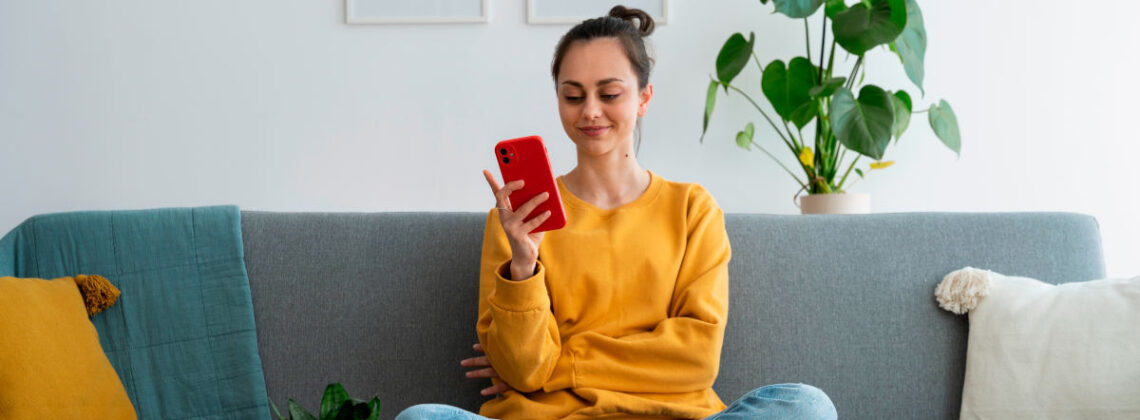 Junge Frau sitzt auf dem Sofa und hat ein Smartphone in der Hand, Symbolbild für einfache Adressänderung bei der Sparkasse Bremen