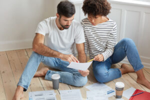 Zwei Menschen sitzen auf dem Boden und gucken sich diverse papiere an, neben stehen zwei Kaffeebecher, Symbolbild für den einfachen Umzugsservice der Sparkasse Bremen