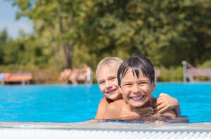 Zwei Kinder schwimmen und lachen im Schwimmbecken eines Freibads