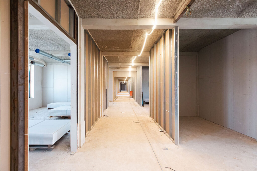 Langer Flur im Rohbau des künftigen Berufsschulcampus Blumenthal mit offenen Metallständerwänden und abgelegten Gipskartonplatten.