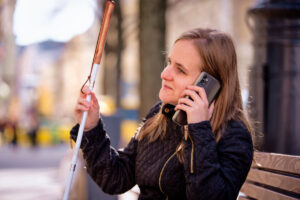 Blinde Frau hält ihren Blindenstock fest und hört etwas mit dem Handy am Ohr