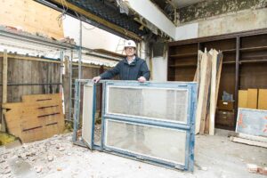 Architekt Michael Schröder auf der Baustelle mit einem großen, blau gerahmten Fenster.