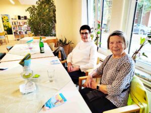 Zwei Seniorinnen sitzen beim Klönschnack im Begegnungszentrum Grambke am Tisch und lächeln. 