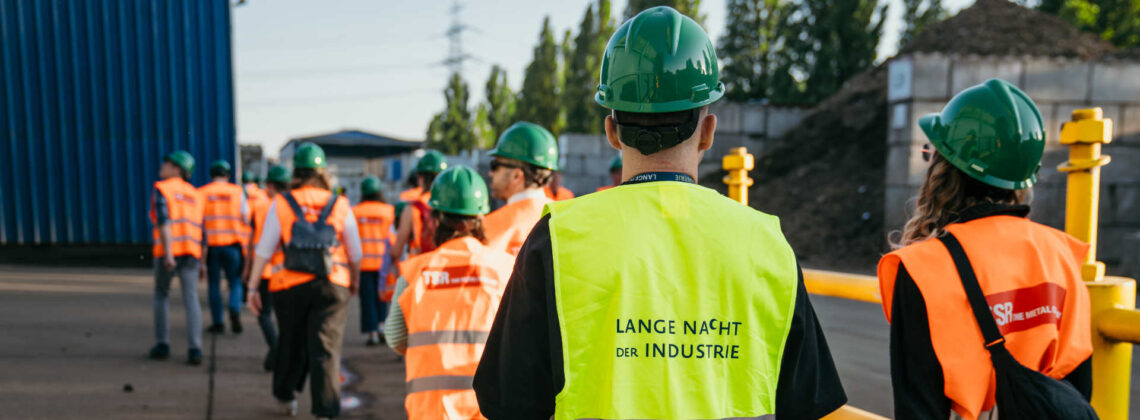 Menschen in Warnweste und Bauarbeiterhelmen laufen über einen Platz bei der Langen Nacht der Industrie