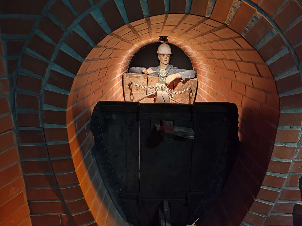 Blick in einen gemauerten Abwasserkanal, in dem eine Puppe einen Karren schiebt.