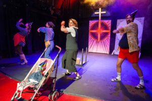 Szene aus dem Theaterstück „Adams Äpfel“ im Schnürschuh Theater: Fünf Darstellerinnen und Darsteller tanzen mit Partyhüten auf der Bühne, im Vordergrund ein Kinderwagen mit einer Puppe