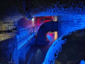 Blick auf einen unterirdischen Kanal und riesige, blau beleuchtete Rohre im Alten Pumpwerk Findorff