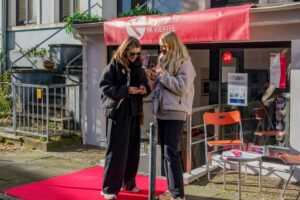 KunstWerk im Viertel: zwei Frauen stehen auf einem roten Teppich und studieren auf den Smartphones den Rundgang zu den Offenen Ateliers