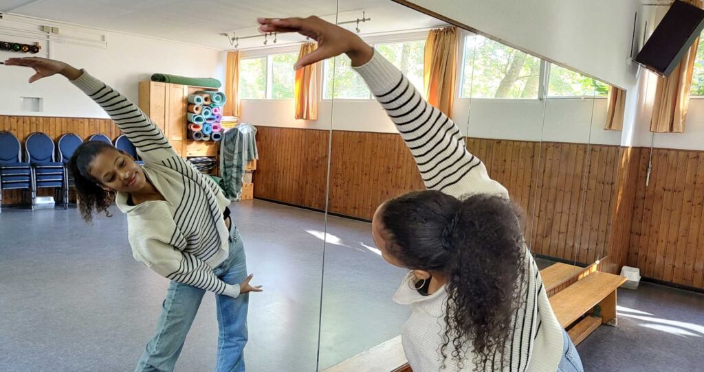 Die Tanzlehrerin Zami Ola Inoussa bietet Tanzkurse für Kinder in Bremen Nord an. Das Foto zeigt sie, wie sie vor dem Spiegel Tanzschritte macht und lächelt.