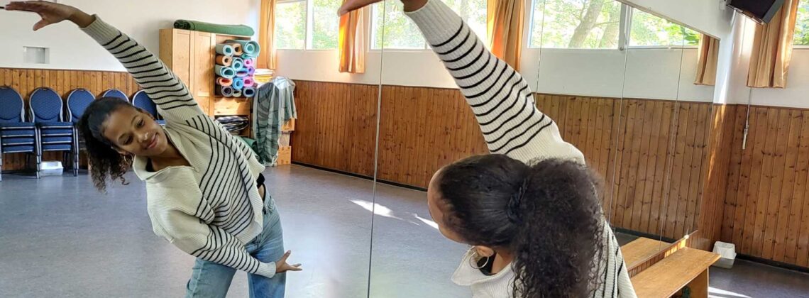 Die Tanzlehrerin Zami Ola Inoussa bietet Tanzkurse für Kinder in Bremen Nord an. Das Foto zeigt sie, wie sie vor dem Spiegel Tanzschritte macht und lächelt.