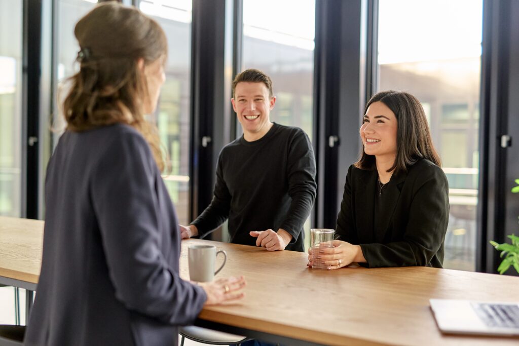 Bild von drei Personen, die sich unterhalten, mit einem Wasser und Kaffee in der Hand