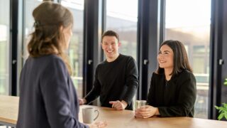Bild von drei Personen, die sich unterhalten, mit einem Wasser und Kaffee in der Hand