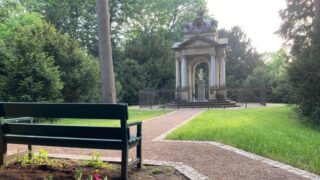 Parkanlage mit einer Bank, Blumen, Blumen, Büschen und Denkmal