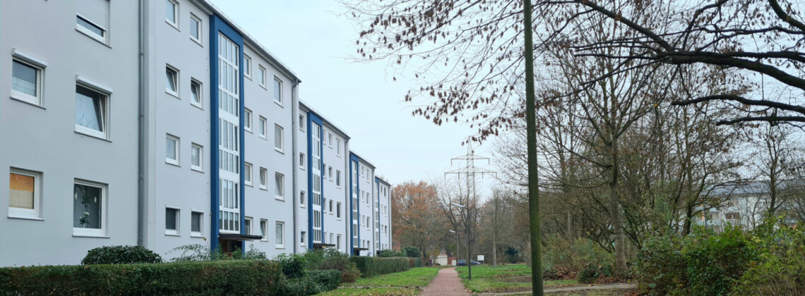 Eine Aufnahme von mehreren Wohnblöcken in Marßel, ein Weg führt entlang der aneinander gereihten Mehrfamilienhäusern entlang, daneben Büsche und Bäume.