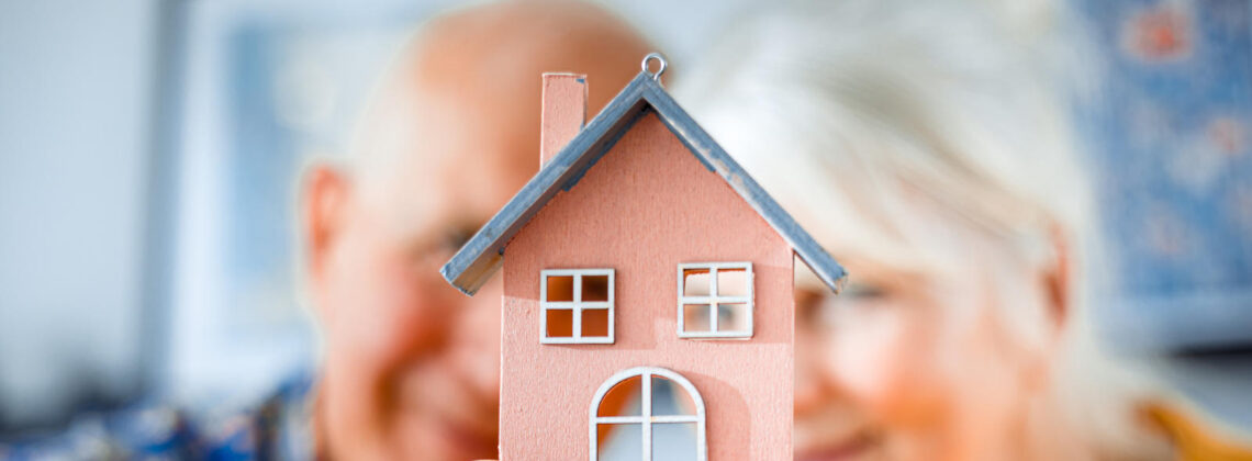 Zwei ältere Menschen halten ein kleines Häuschen in die Kamera, Symbolbild für Pflegeimmobilien