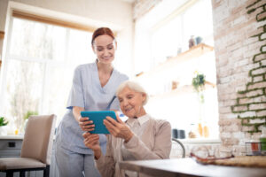 Pflegekraft kümmert sich um eine ältere Frau, die ein Tablet in der Hand hält