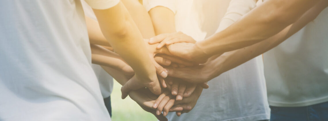 Symbolbild für den Internationalen tag des Ehrenamtes, viele Menschen strecken ihre Hände in der Mitte zusammen