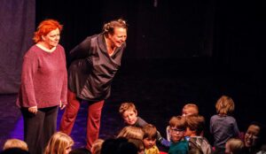Zwei Schauspielerinnen stehen lächelnd auf der Bühnen, davor ist ein Publikum aus Kindern zu sehen. Das Foto stammt aus einer Theateraufführung beim Tag for Lütte im Zentrum für Kunst Bremen.