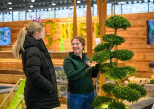 Eine Frau lässt sich auf der Hansebau von einer lächelnden Gärtnerin eine Pflanze erklären.