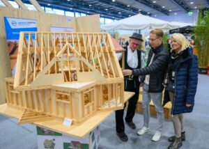 Ein Paar lässt sich bei der Messe Hansebau von einem Handwerke in Arbeitskleidung ein Hausmodell aus Holu erklären.