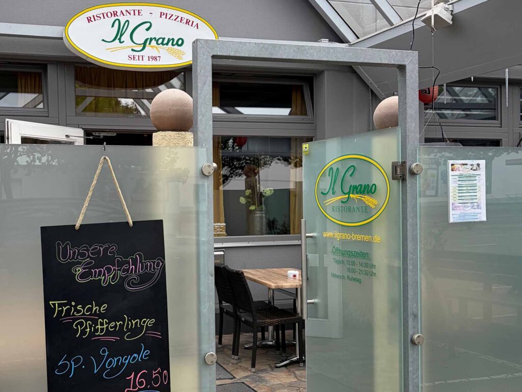 Geöffnetes Glastor des Restaurants Il Grano mit Logo und handgeschriebener Angebotstafel