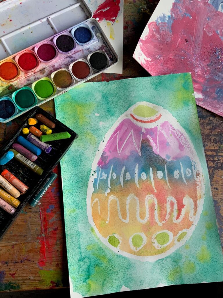 Gemaltes Bild eines Ostereis mit einem Tuschkasten und Wachsmalstiften