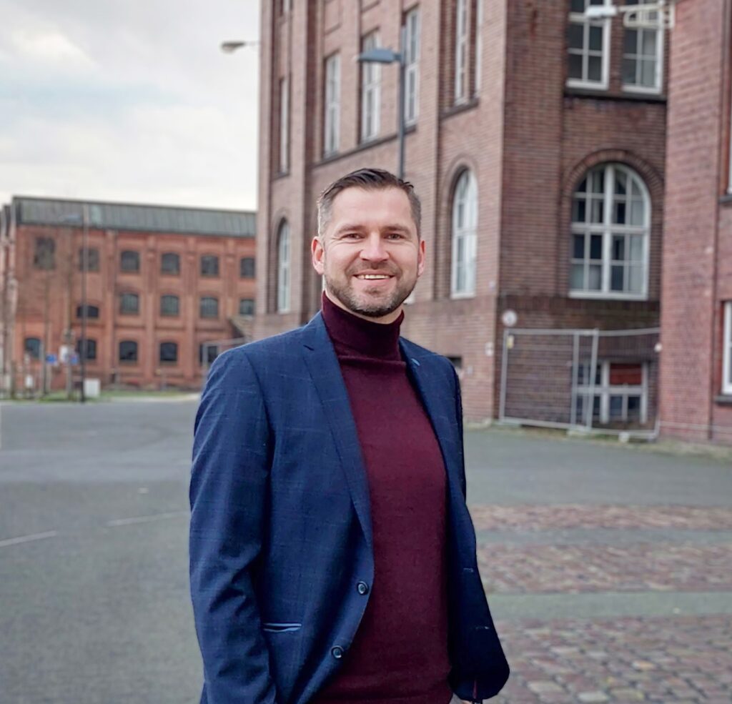 Ein Mann lächelt. Steht vor denkmalgeschützten Gebäude