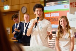 Jugendliche präsentieren auf einer Bühne ihre Projektidee beim Wettbewerb YES! Young Economics Solutions.