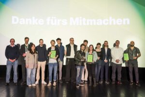 Gruppenfoto von Teilnehmenden und ausgezeichneten Filmschaffenden auf einer Bühne vor einer Leinwand mit der Aufschrift „Danke fürs Mitmachen“.