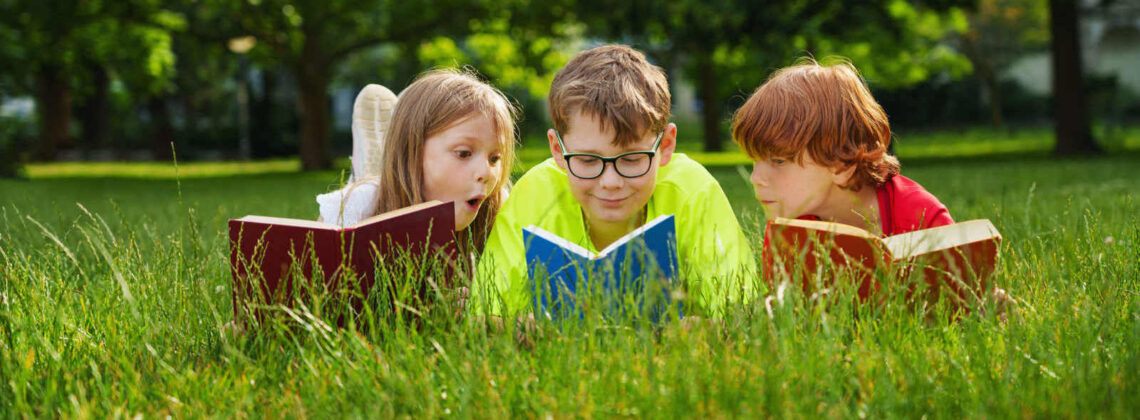 Drei Kinder liegen mit offenen Büchern auf einer Wiese